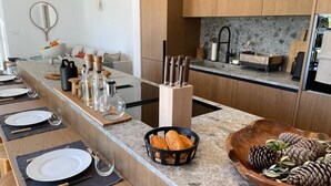 Una cocina moderna con encimera de mármol, armarios de madera y una isla central con un bloque de cuchillos y un cesto de pan.