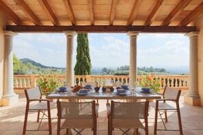 Enjoy a dining experience under a charming pergola with a scenic view of rolling hills and a cypress tree.