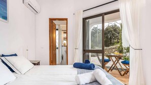 A hotel room with a bed, a small table with a chair, and a balcony with a table and chairs.