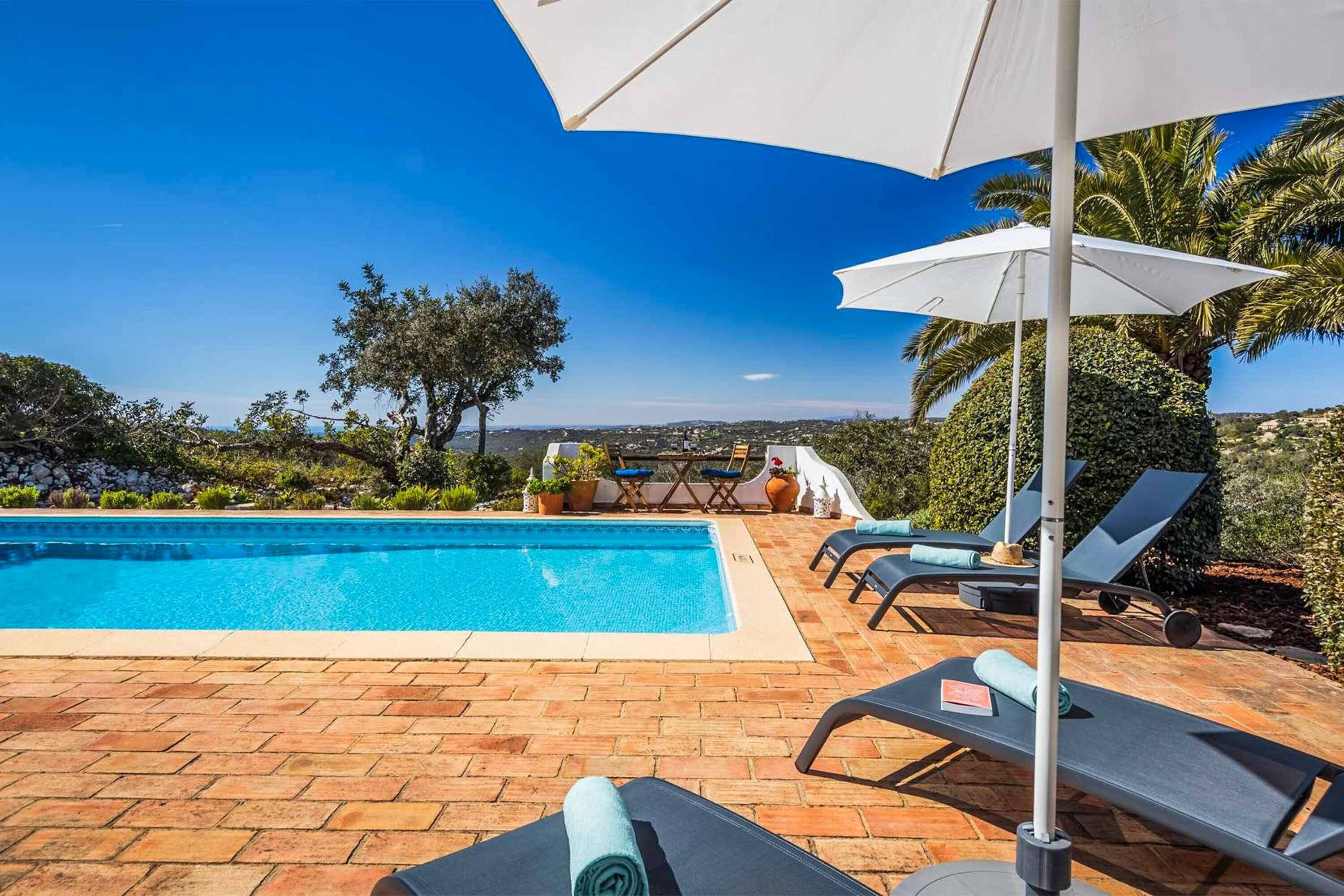Zona junto a la piscina con vista despejada del paisaje, incluyendo árboles y una vista distante de un pueblo.