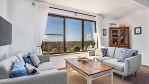 A living room with two grey sofas, a wooden coffee table, and a large window with a view of the landscape.