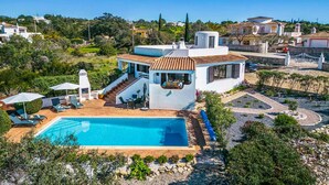 A modern villa with a swimming pool, outdoor seating, and a view of the surrounding landscape.