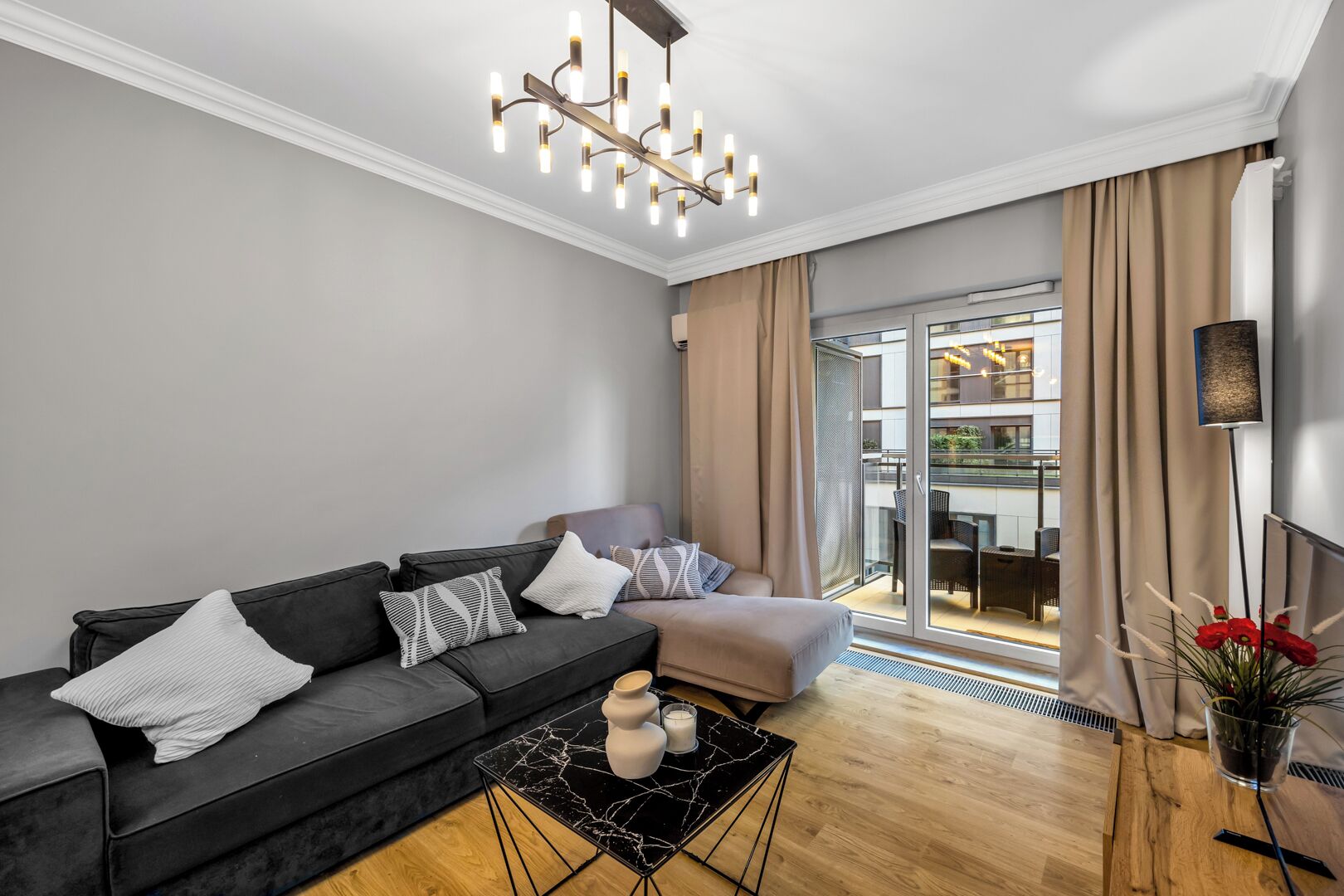 A modern living room with a black sofa, a glass door leading to a balcony, and a black marble coffee table.