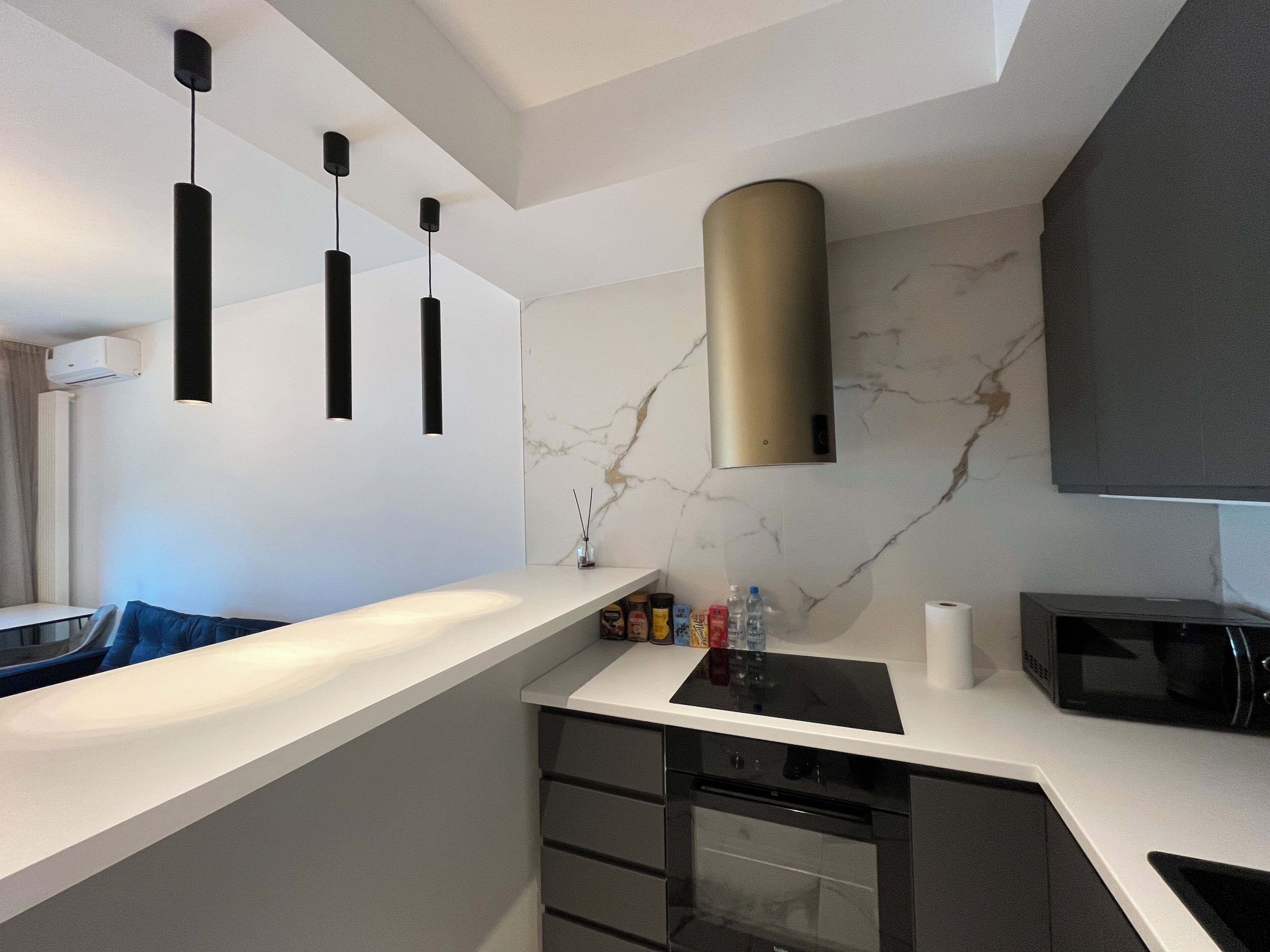 Una cocina moderna con encimera blanca, armarios negros, extractor de acero inoxidable y microondas negro.