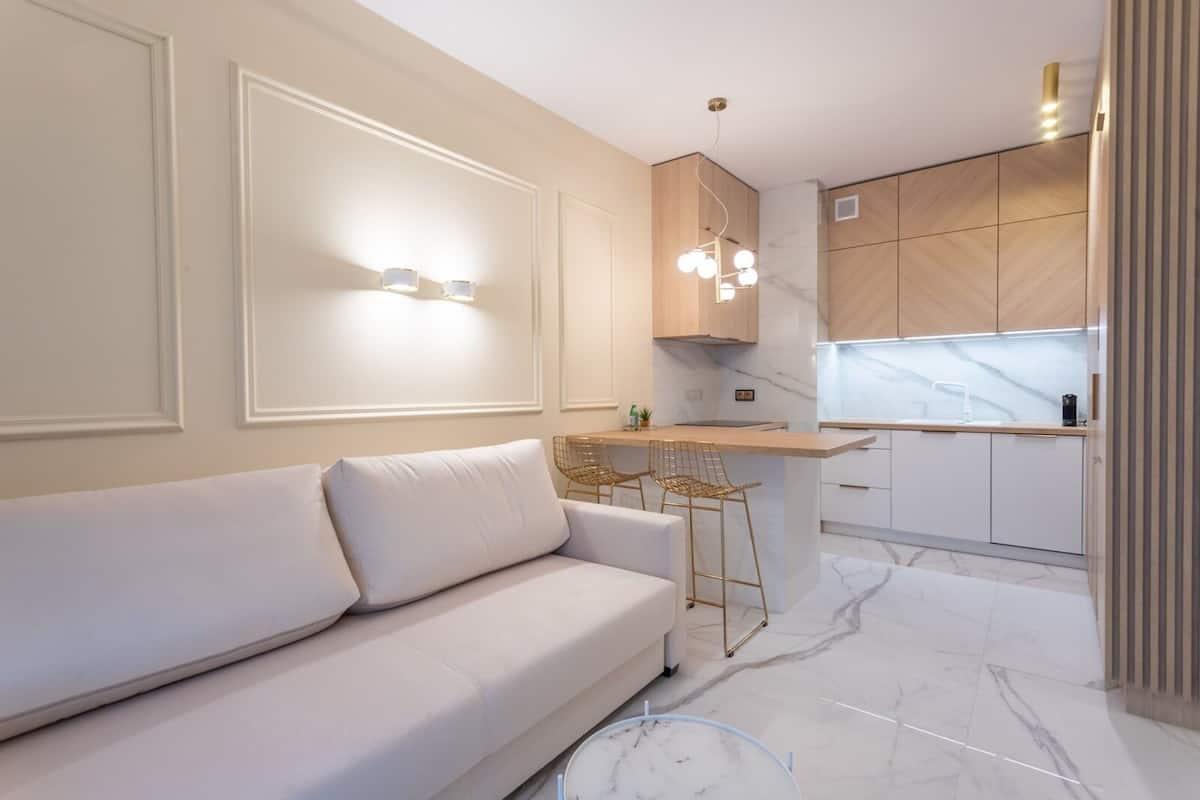 A modern kitchen with a white sofa, wooden cabinets, and a marble floor.