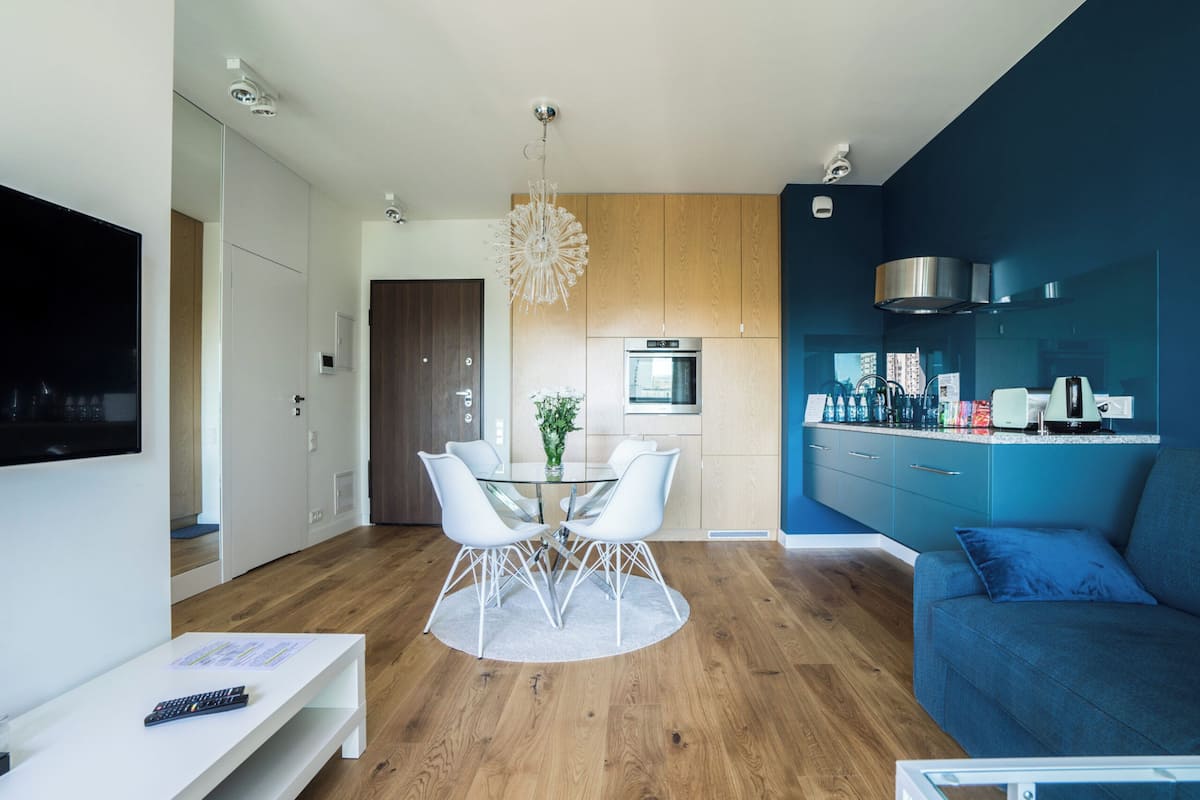 A modern living room with a TV, a dining table with chairs, a sofa, and a kitchen area with cabinets and appliances.