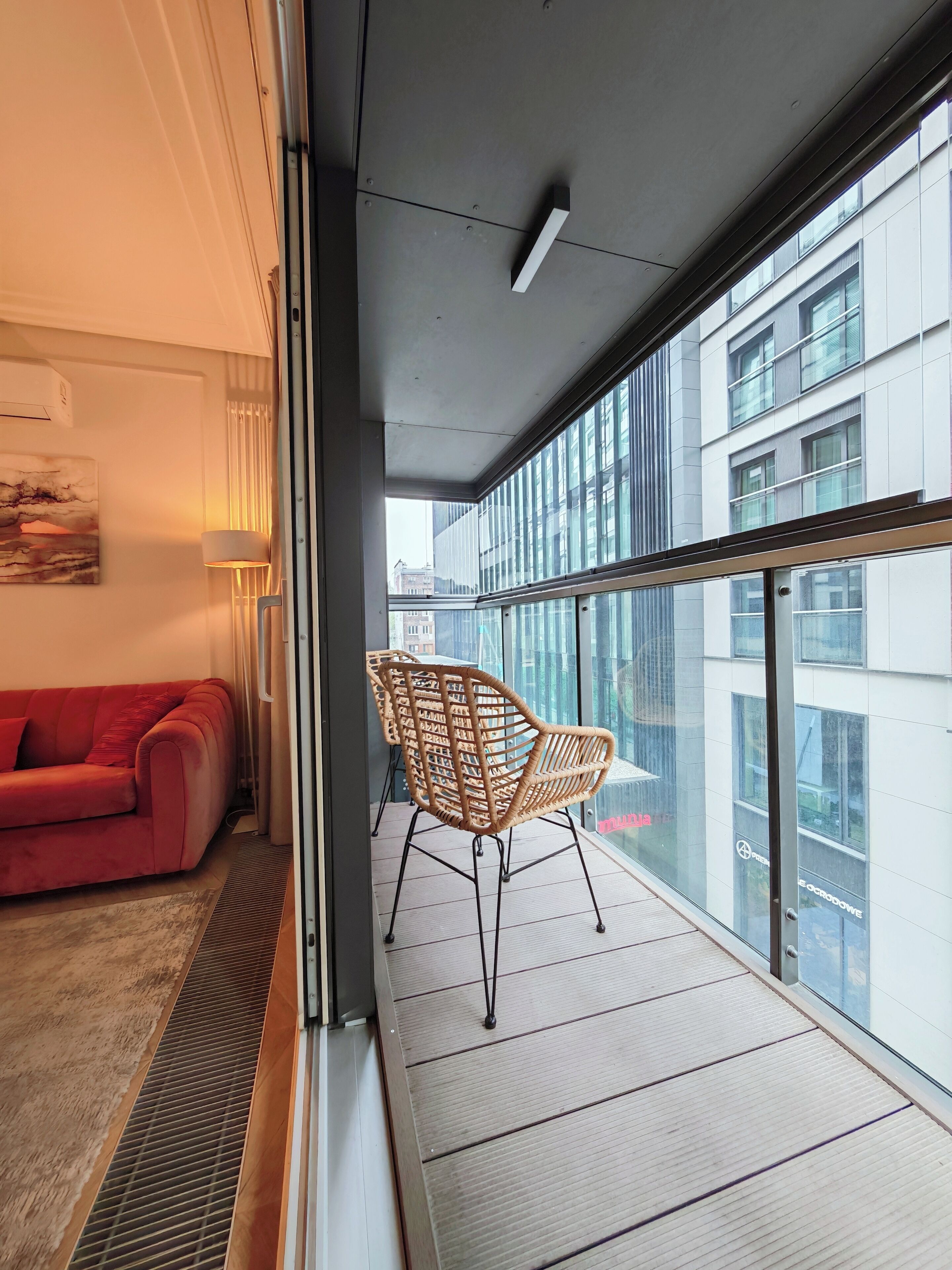 Et moderne hotelværelse med en rød sofa, en fletstol og store vinduer med udsigt over byen.