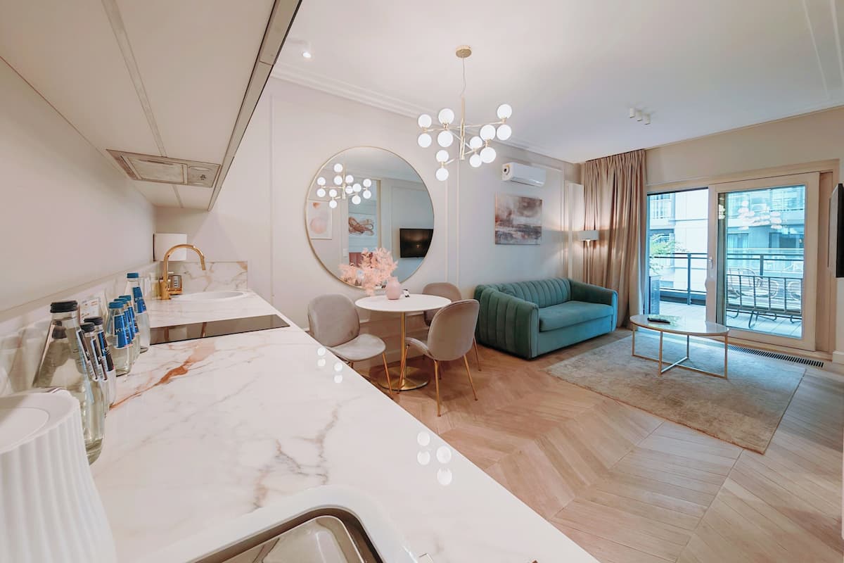 A modern hotel room with a marble vanity, round mirror with lights, a green sofa, and a balcony with a view.