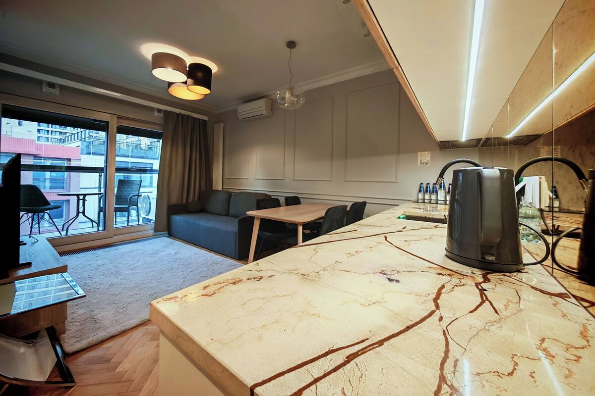 A modern kitchen with a marble countertop, a coffee machine, and a dining area with a sofa and chairs.