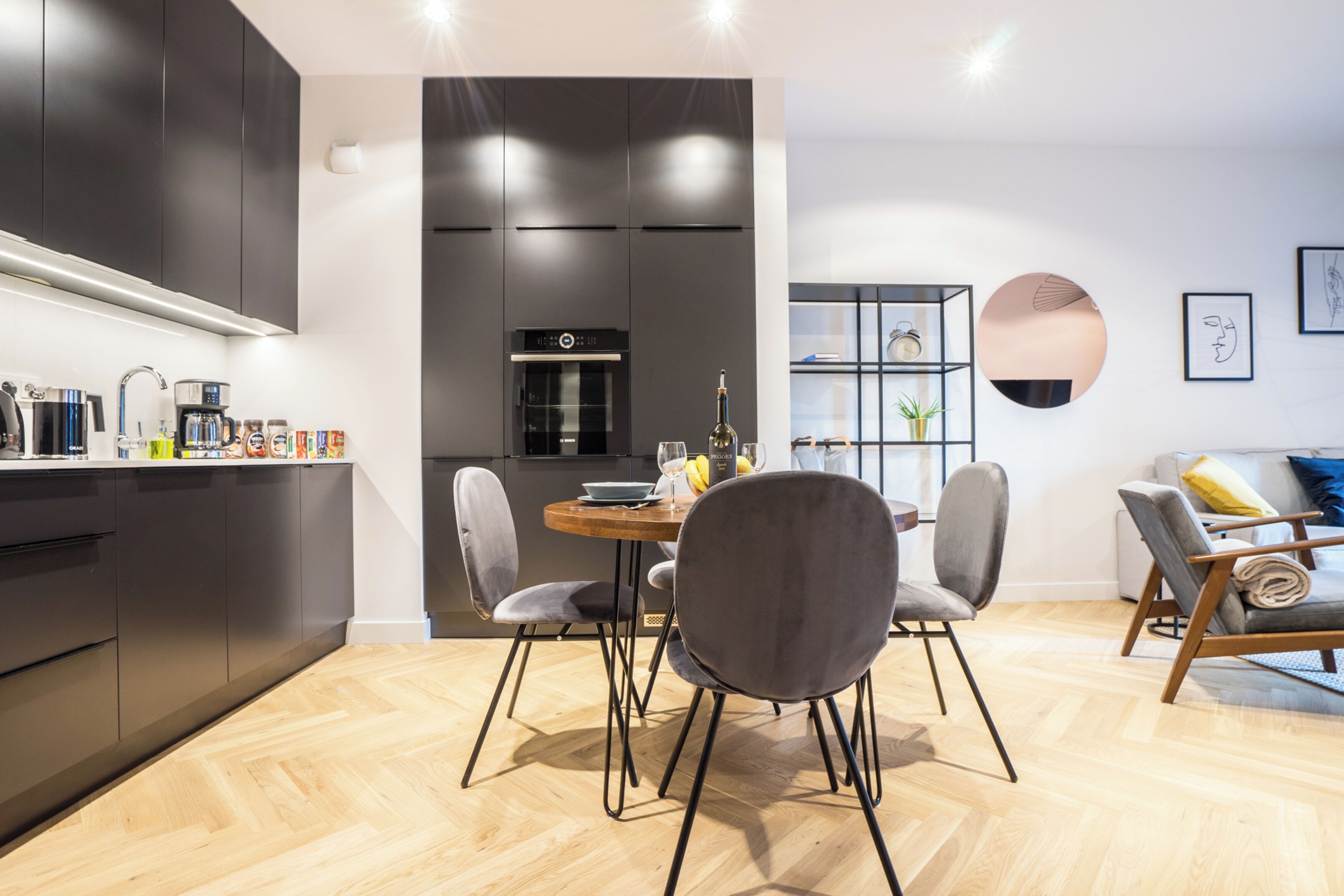 Une cuisine moderne avec des meubles de couleur sombre, un îlot central et un coin repas doté de chaises grises.