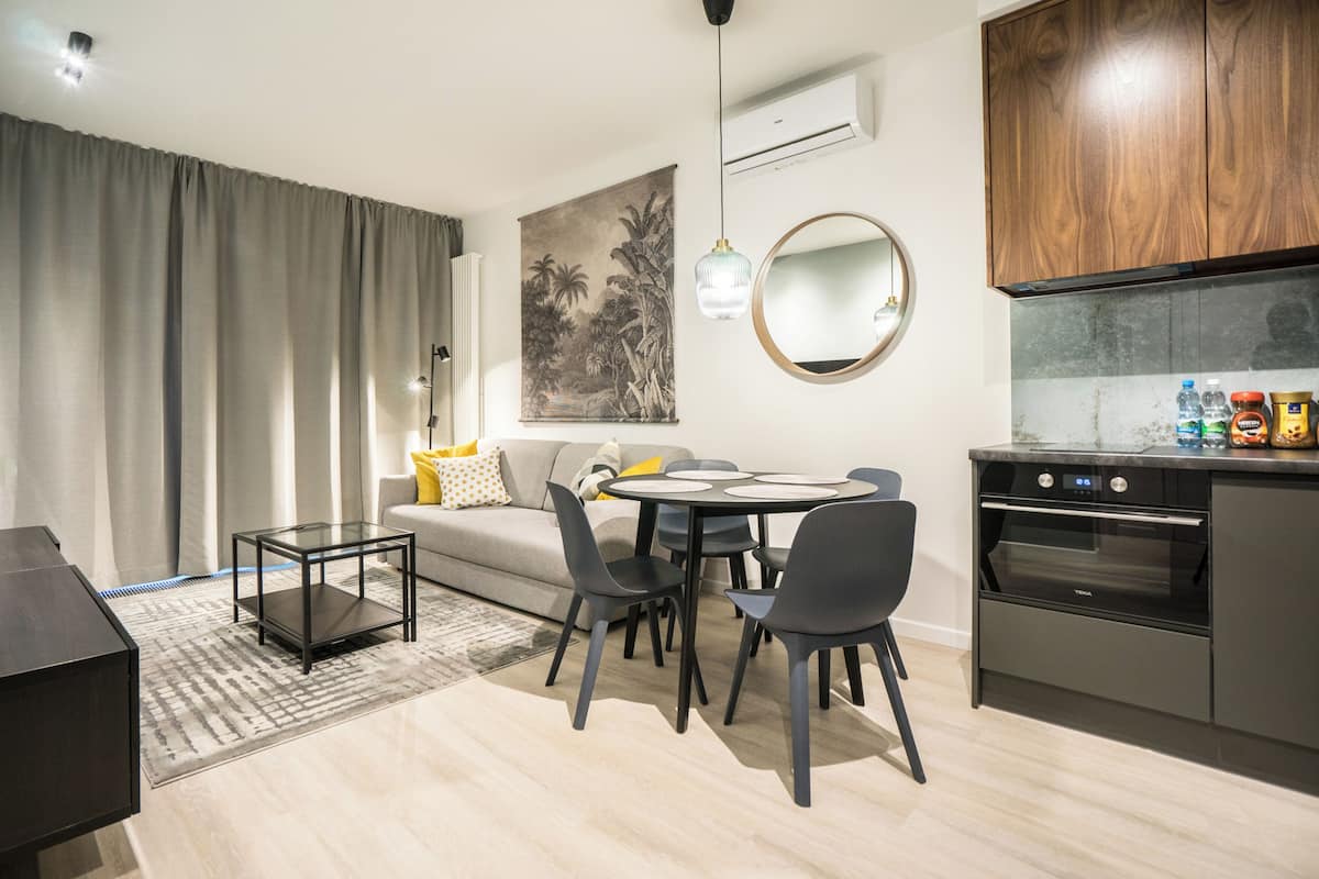 A modern living room with a sofa, dining table, chairs, and a kitchen area with an oven.