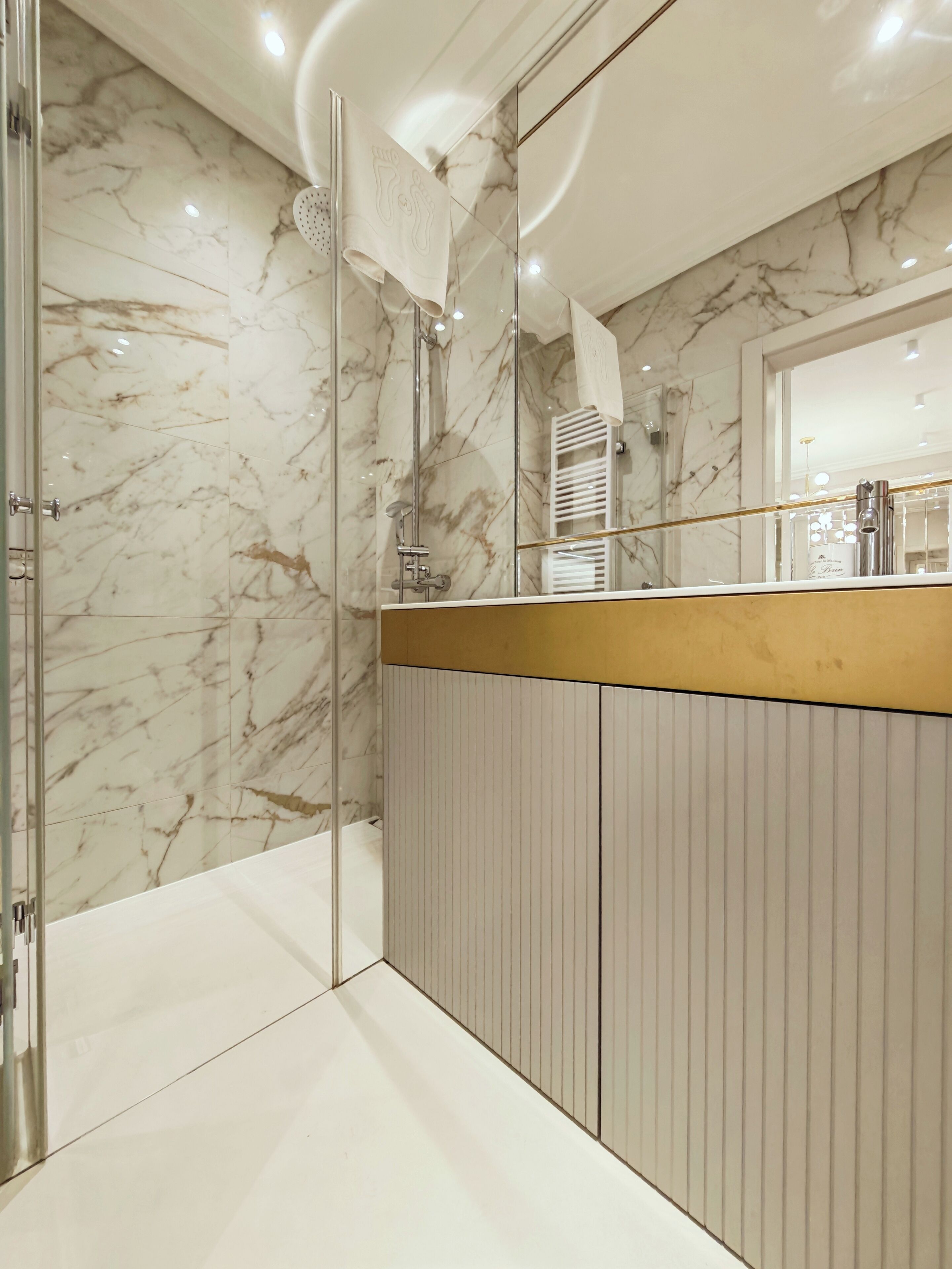 Un baño moderno con cabina de ducha de vidrio, paredes de mármol y tocador de madera con espejo.