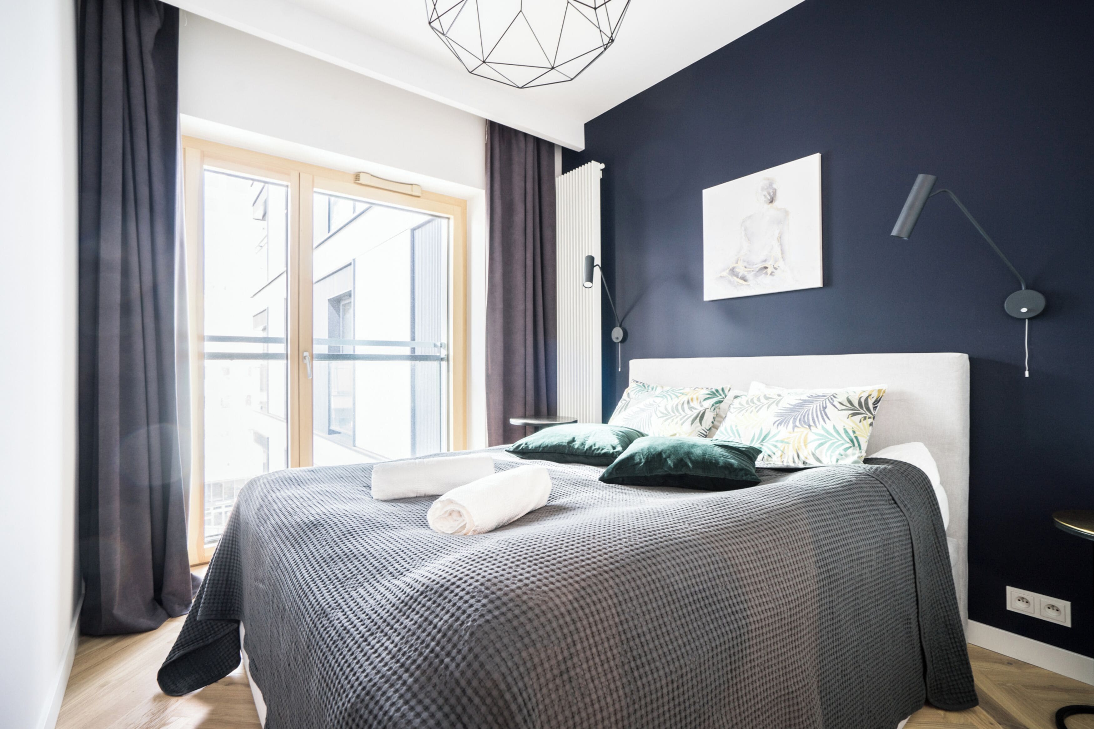 A modern bedroom with a large bed, dark walls, and a window with curtains.