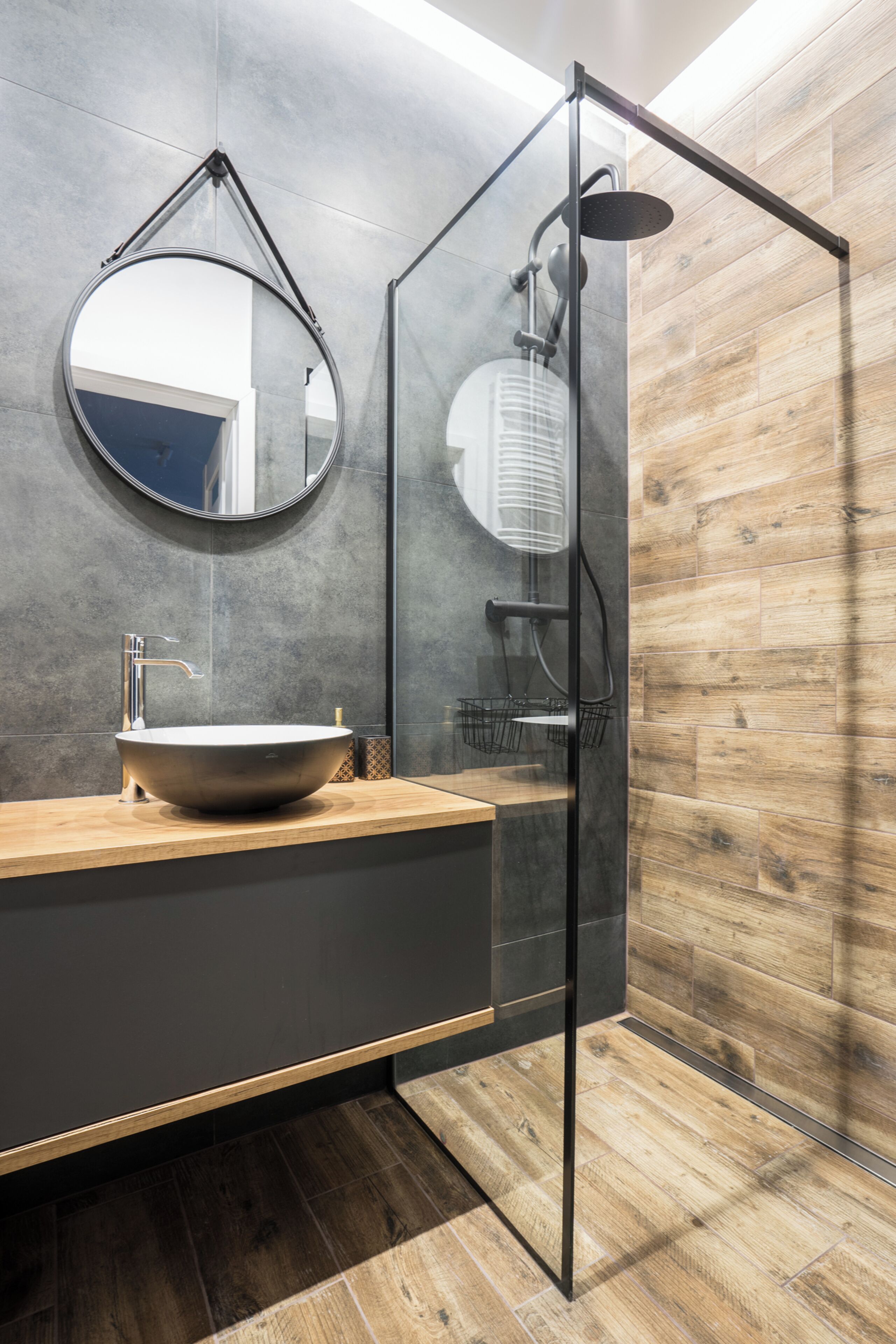 A modern bathroom with a round mirror, a vessel sink, and a glass-enclosed shower.