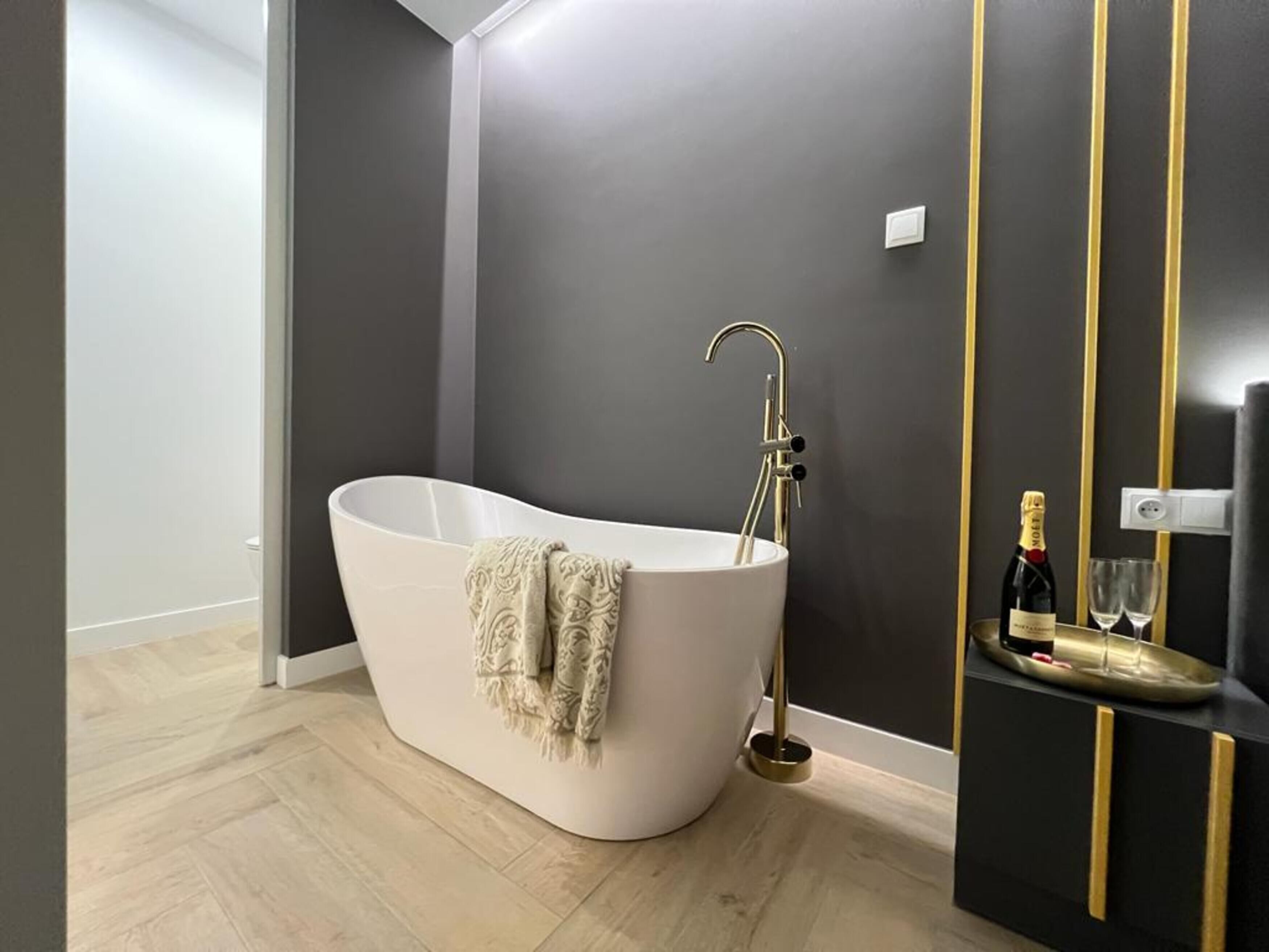 Ein modernes Badezimmer mit einer freistehenden Badewanne, einem goldenen Wasserhahn und einem kleinen Regal mit einer Flasche und Gläsern.