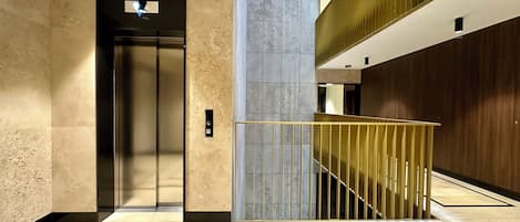 A modern elevator with a metallic finish, a marble wall, and a wooden panel on the right.