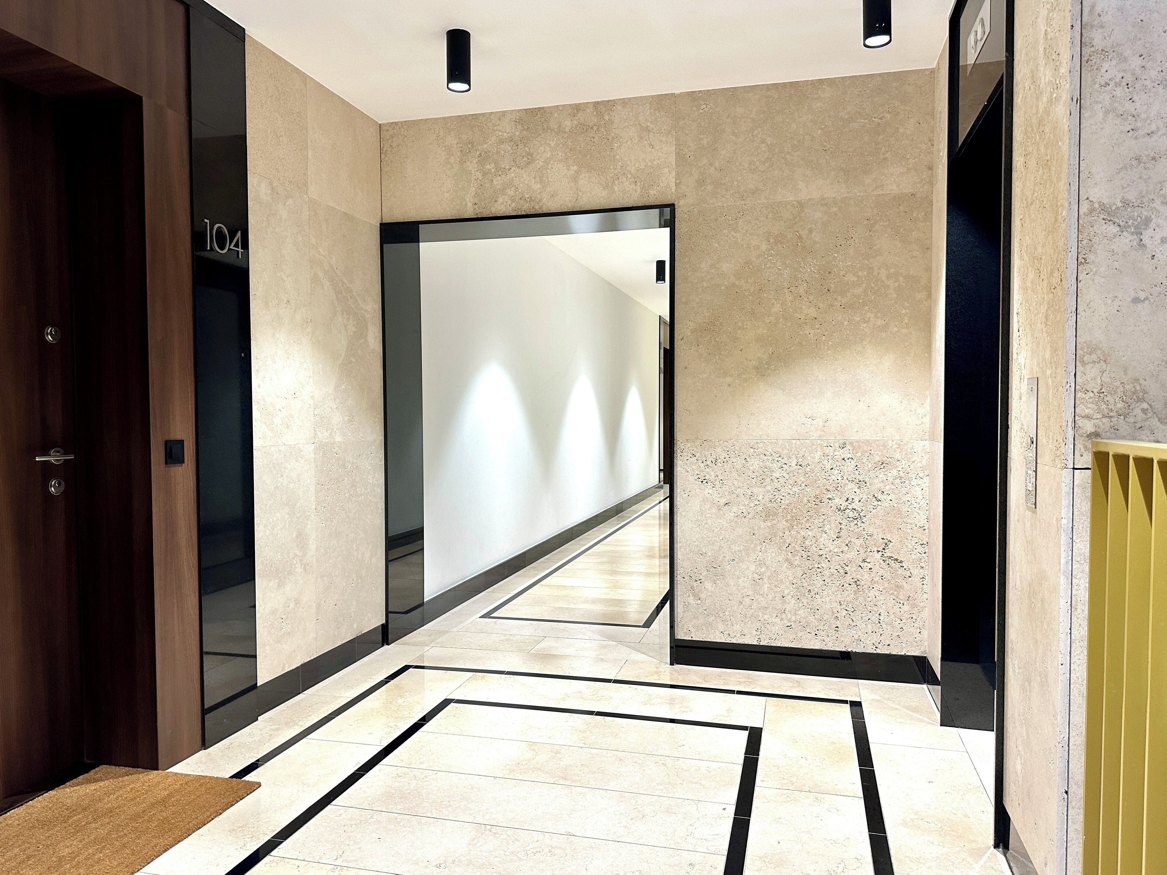 A modern hallway with a marble floor, a wooden door, and a glass door leading to another room.