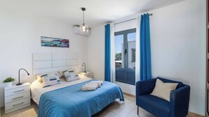 Een slaapkamer met een bed, nachtkastjes, een lamp, een stoel en een raam met gordijnen.