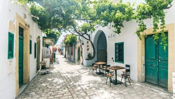 A narrow cobblestone street with white buildings, green shutters, and outdoor seating. - Dar Tobbel Borj Errass Mahdia (Mahdia)