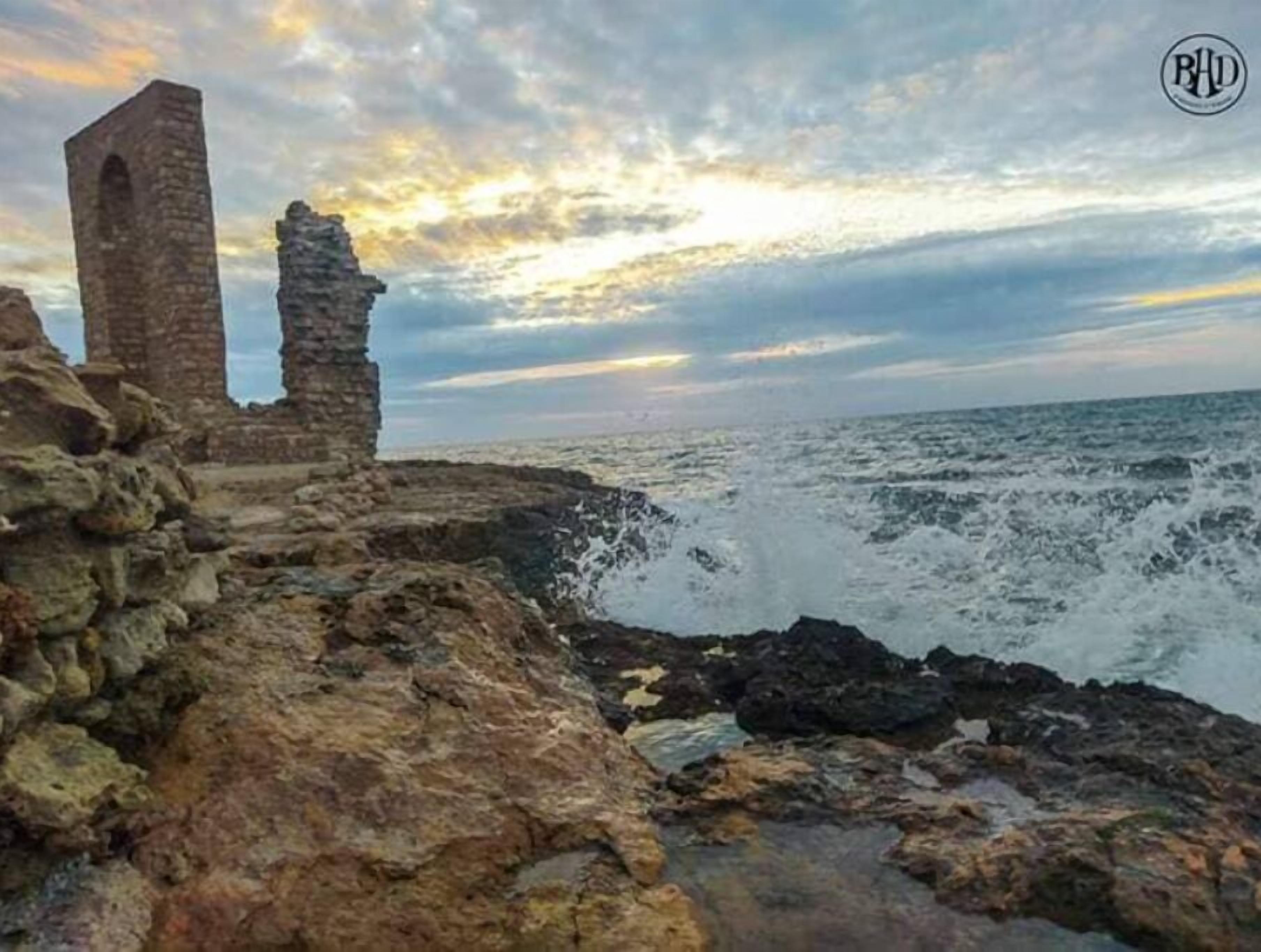 De vieilles ruines de pierre au bord de la mer, où les vagues s'écrasent contre les rochers.