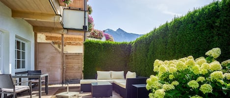 A wooden deck with outdoor furniture, a hedge, and a mountain in the background.