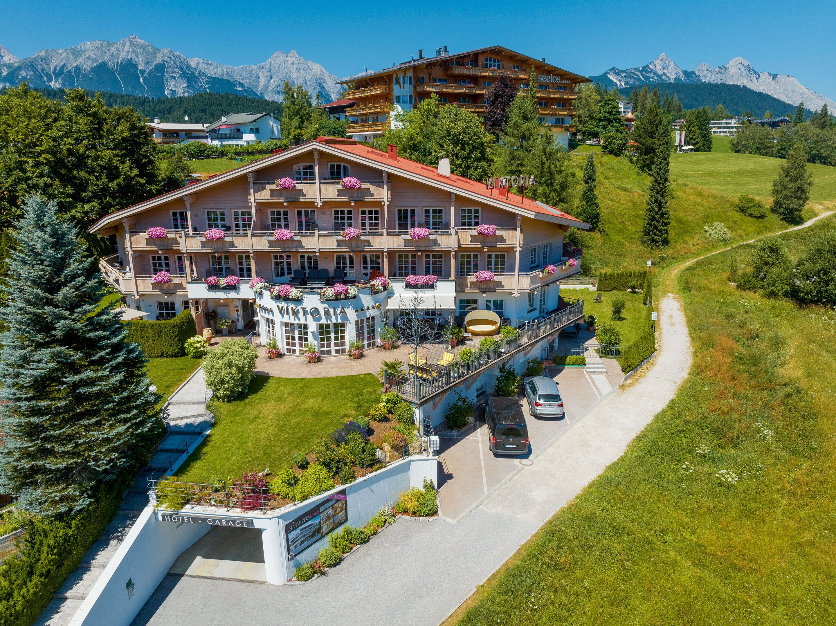 Ein Hotel mit einem großen Gebäude, Balkonen mit Blumenkästen, einer sichtbaren Garage und einem Weg zum Eingang.