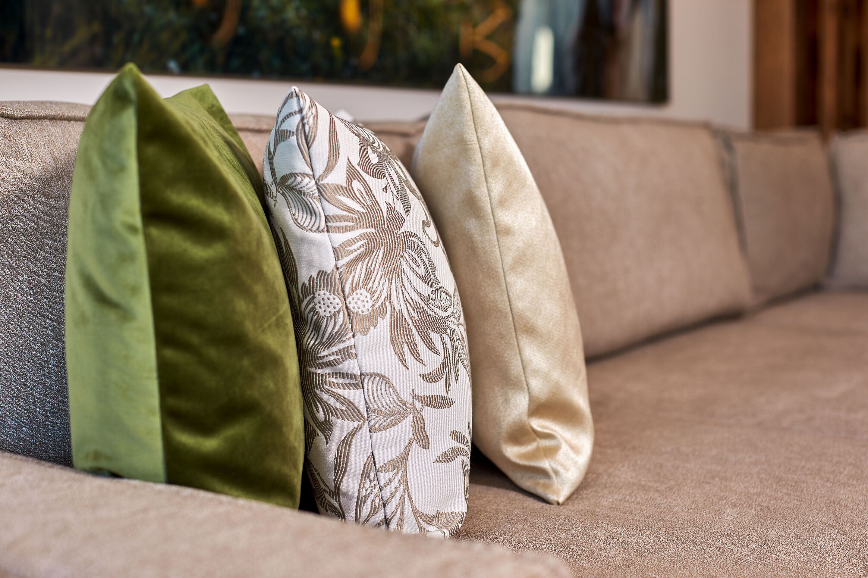 A beige sofa with three pillows in different colors and patterns.
