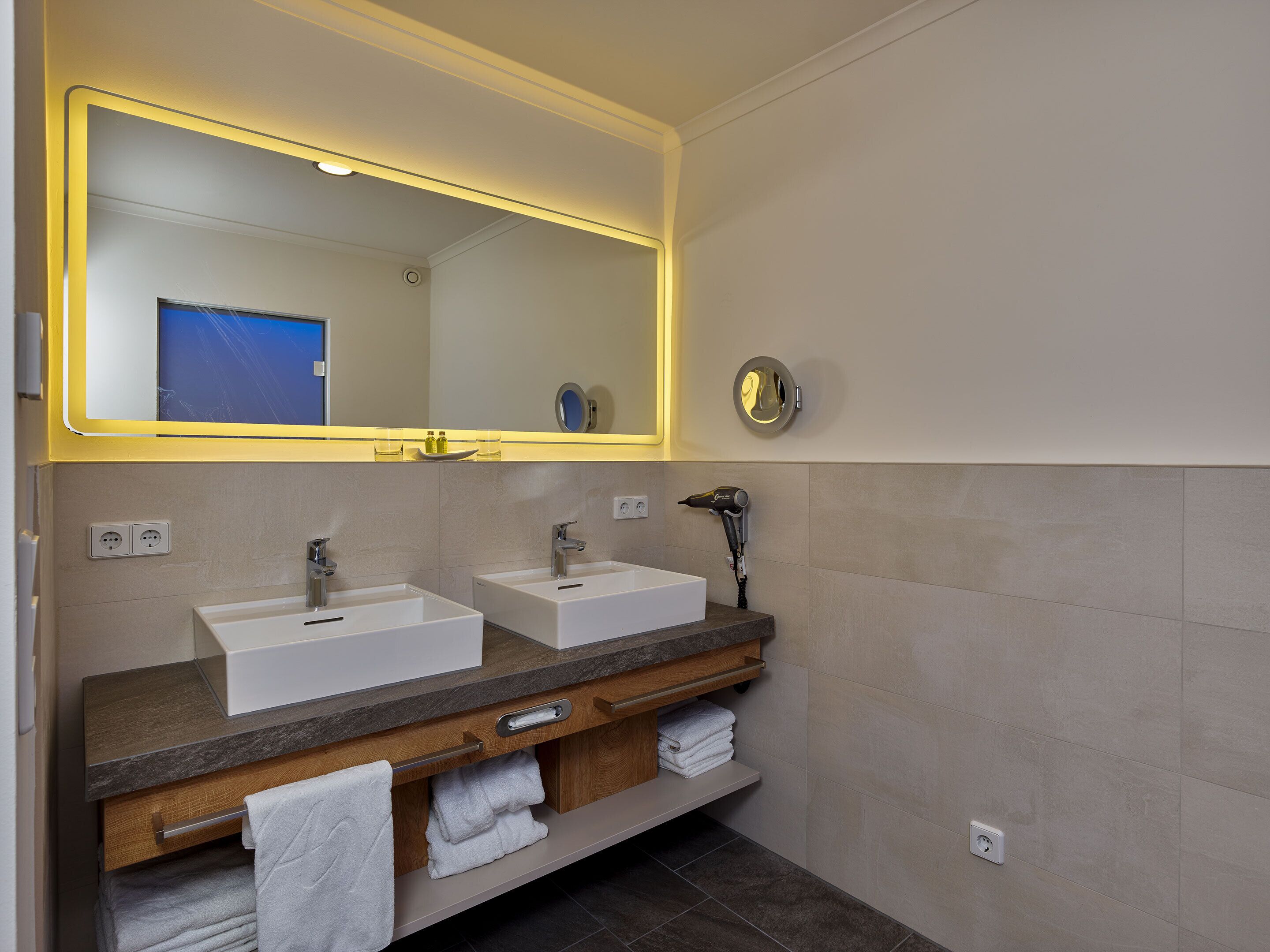 Een moderne badkamer met twee wasbakken, een spiegel en een haardroger.