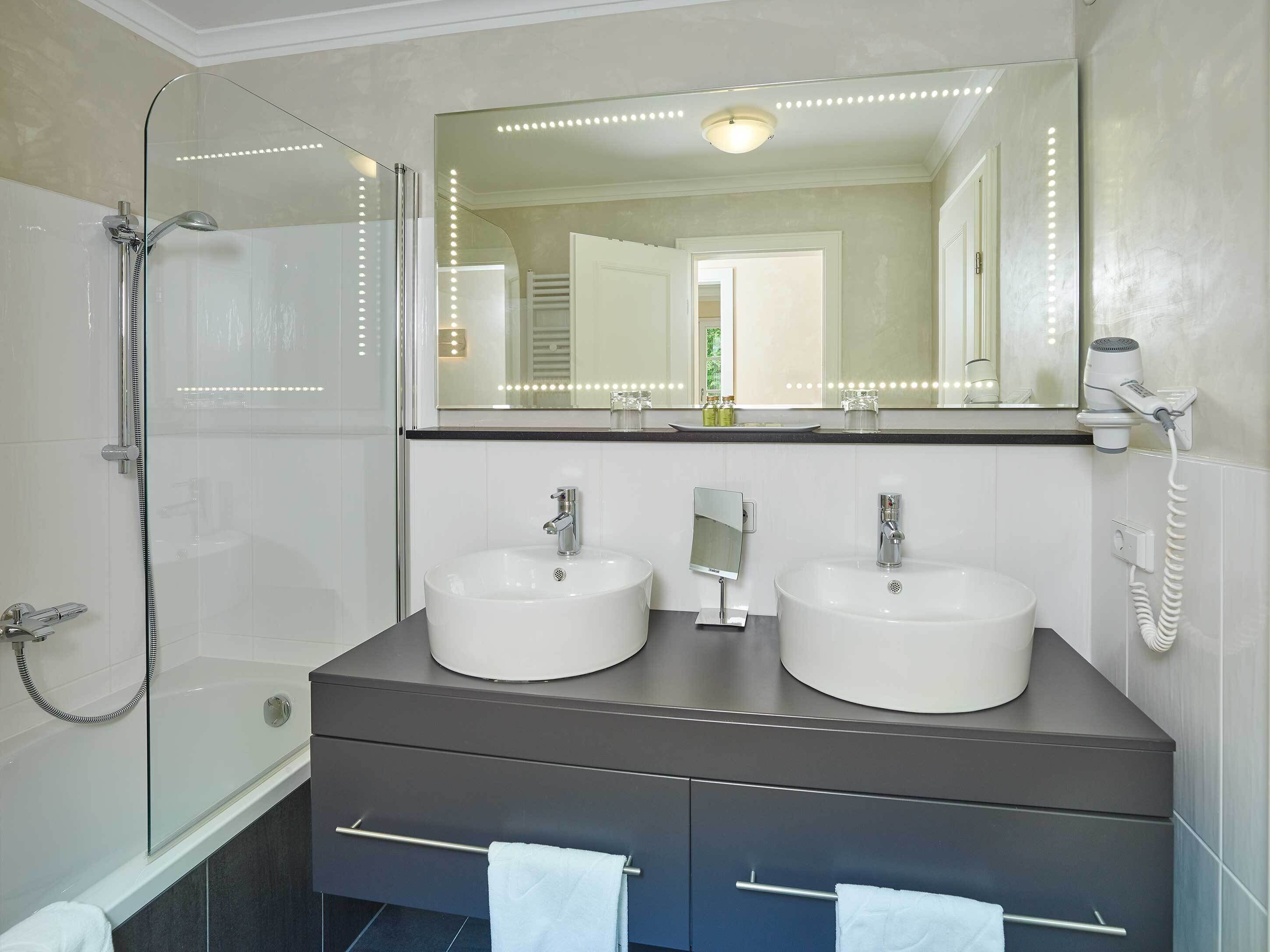 Une salle de bain moderne avec deux vasques, une douche en verre et un grand miroir doté de lumières à LED.