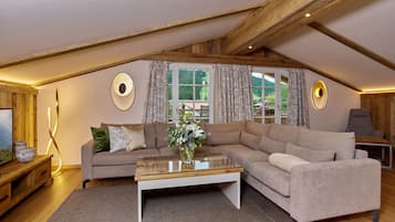 A cozy loft-style living room with a large sectional sofa, a glass coffee table, and a wooden ceiling.