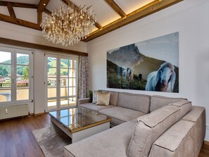 A modern living room with a glass coffee table, beige sofa, and a large painting of horses.