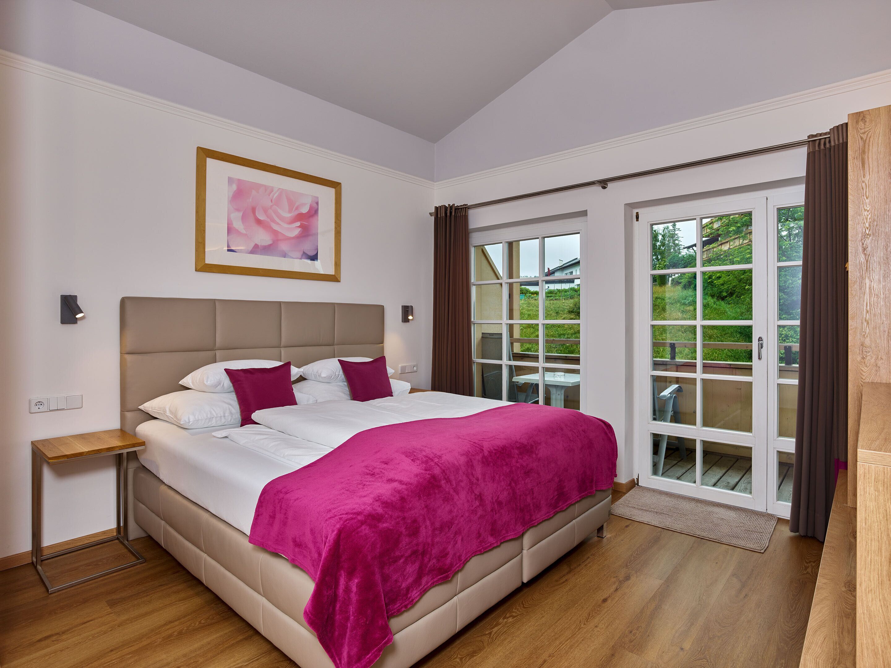 A bedroom with a bed, a nightstand, a window with curtains, and a door leading outside.
