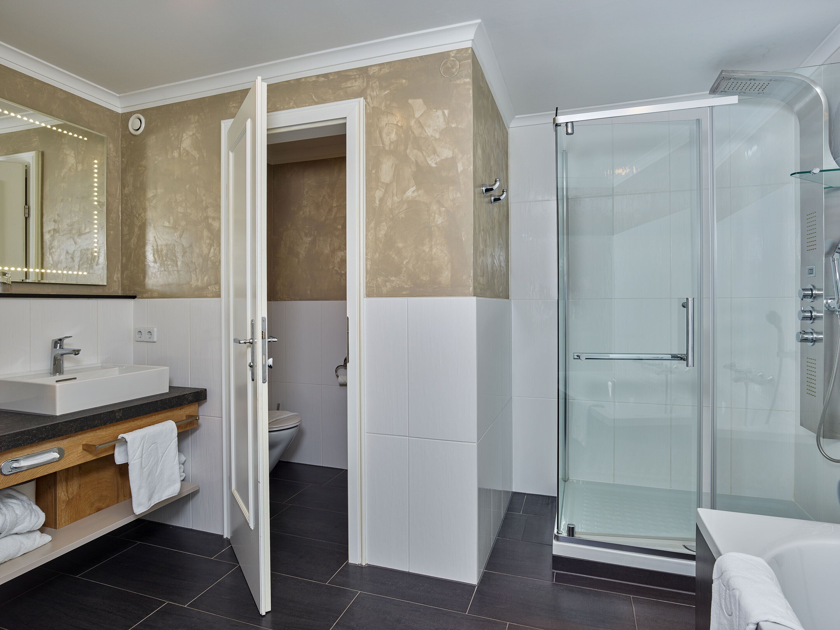 Ein modernes Badezimmer mit Duschkabine, Waschtisch und Toilette, die durch eine offene Tür sichtbar ist.