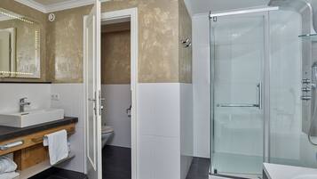Ein modernes Badezimmer mit Duschkabine, Waschtisch und Toilette, die durch eine offene Tür sichtbar ist.