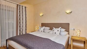 A bedroom with a large bed, two bedside tables, a wooden nightstand, and a wall-mounted light fixture.