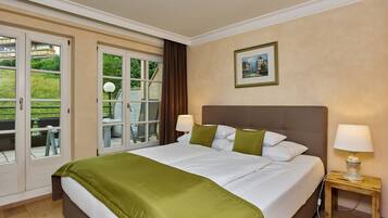 Habitación de hotel con una cama grande, dos lámparas de noche, una mesita con lámpara, un cuadro enmarcado en la pared y un ventanal corredero que da a un espacio exterior con mesa y sillas.