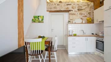 A compact kitchen with white cabinets, a wooden ceiling, and a stone wall.