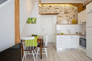 A compact kitchen with white cabinets, a wooden ceiling, and a stone wall. - Polyxenis Cozy Maisonette - Lefkada BnB (Lefkada)