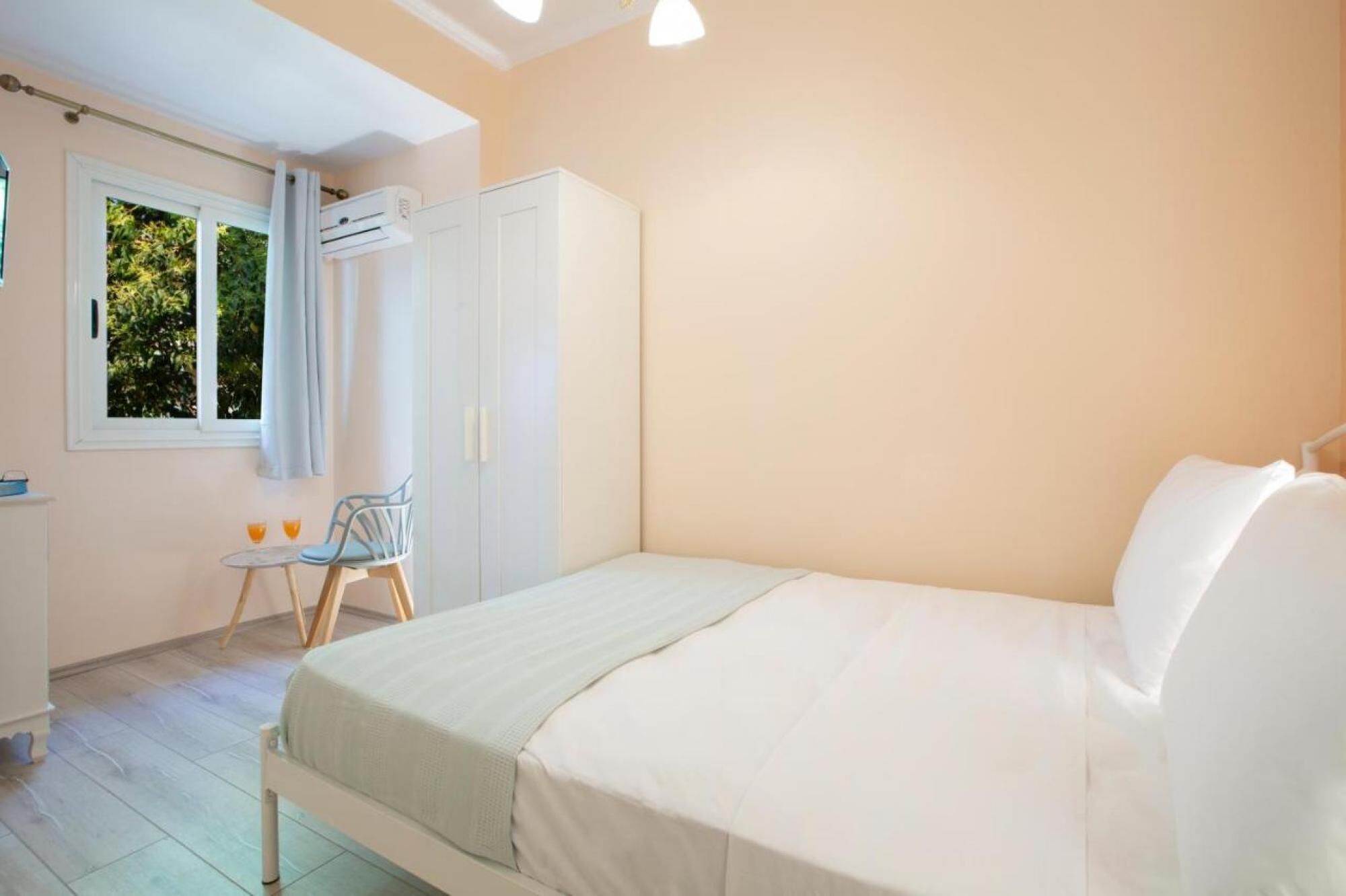 A bedroom with a bed, a wardrobe, a chair, a table with two glasses, and an air conditioning unit.