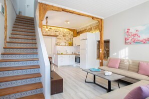 A modern kitchen with white cabinets, a wooden staircase, and a beige sofa with pink cushions. - Polyxenis Cozy Maisonette - Lefkada BnB (Lefkada)