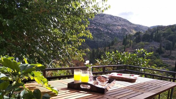 A wooden table with a tray of food and drinks, set against a scenic mountain backdrop. - Aggelos House in Kalamitsi (Lefkada)