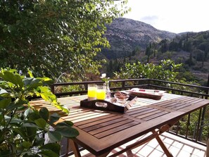 A wooden table with a tray of food and drinks, set against a scenic mountain backdrop. - Aggelos House in Kalamitsi (Lefkada)