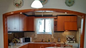 A compact kitchen with wooden cabinets, a microwave, a stove, and a dining table with chairs. - Aggelos House in Kalamitsi (Lefkada)