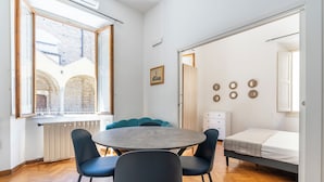 Una habitación con una mesa redonda, cuatro sillas, una cama, un radiador y vistas a un patio exterior.