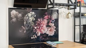 Una habitación con un cuadro floral grande en la pared, un escritorio de madera con una tableta, y una lámpara colgante.