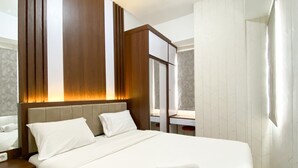 A modern hotel room with a large bed, wooden headboard, and a bathroom with a mirror and white tiles. - Great Choice And Modern 2Br At Transpark Juanda Bekasi Timur Apartment (Bekasi)