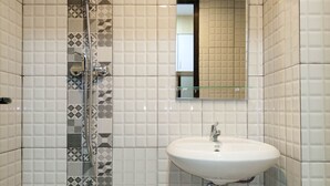 Un baño con un lavamanos blanco, cabina de ducha con mampara de vidrio y azulejos estampados.