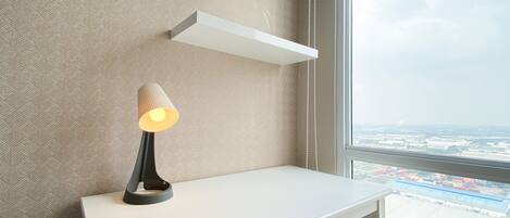 A modern room with a white desk, a lamp, and a view of a port through a large window.