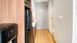 A narrow hallway with a wooden floor, a black refrigerator, and a door with a red sticker.