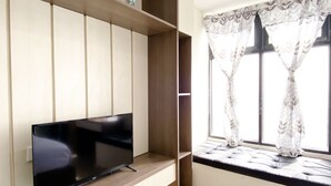 Una sala moderna con un televisor de pantalla plana sobre un estante de madera, una ventana con cortinas estampadas y un banco empotrado con asiento acolchado.